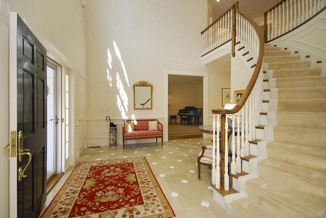 foyer entrance with stairway, a wainscoted wall, and a high ceiling