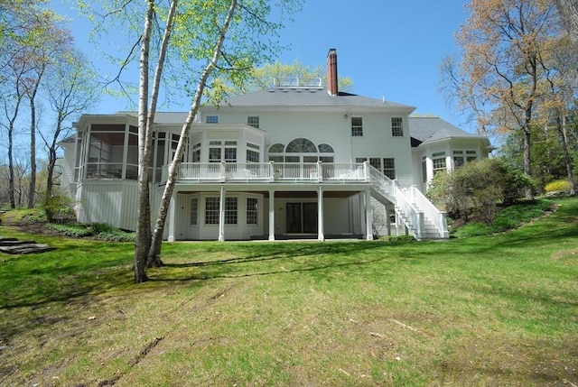 rear view of property with stairs, a sunroom, a chimney, and a lawn