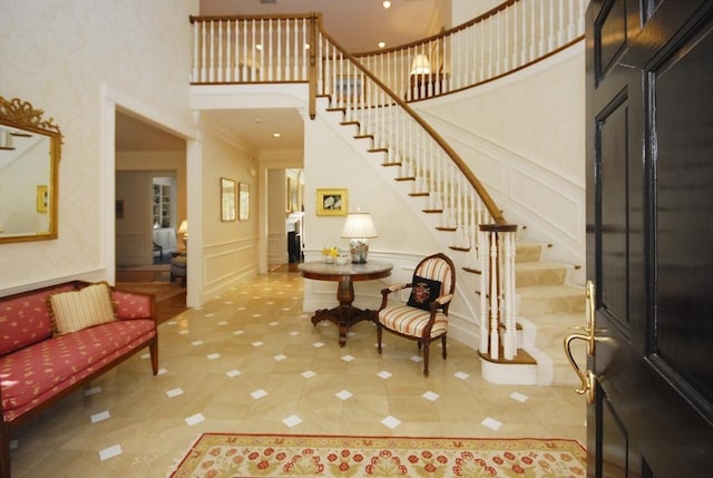 foyer entrance featuring stairway, crown molding, a high ceiling, and a decorative wall