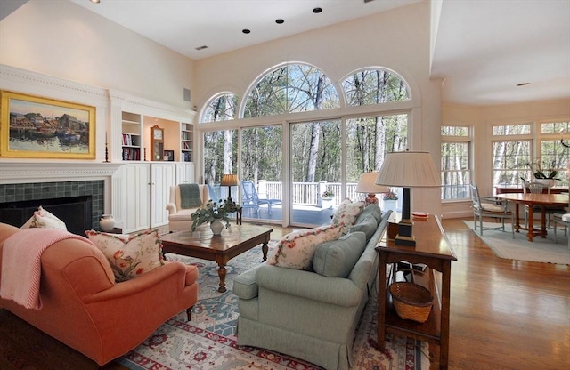 living room featuring a tile fireplace, a wealth of natural light, wood finished floors, and a high ceiling