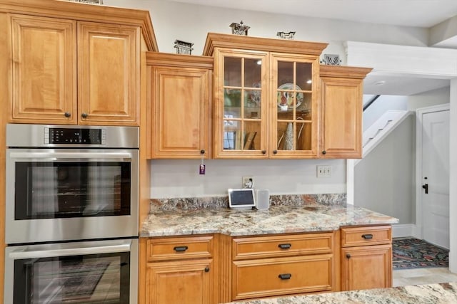 kitchen with double oven, light stone counters, and glass insert cabinets