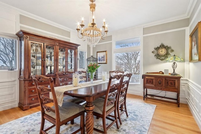 dining area featuring a chandelier, a decorative wall, light wood-style flooring, and crown molding