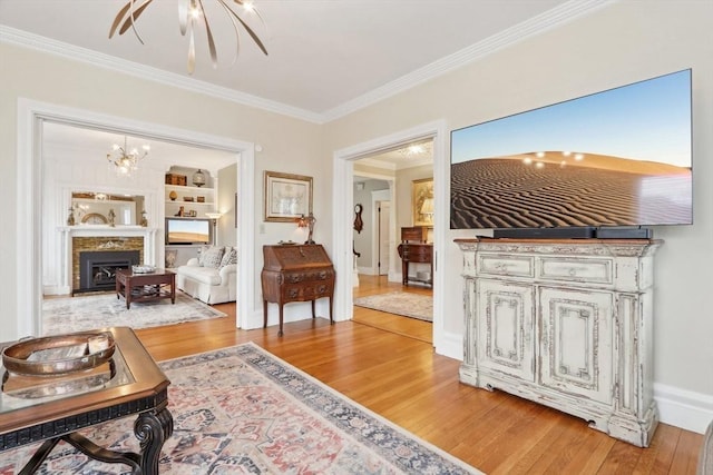 living room with built in shelves, light wood finished floors, a fireplace, ornamental molding, and a notable chandelier