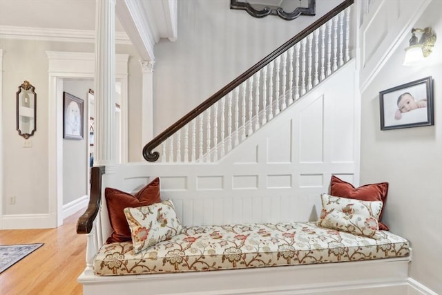 interior space featuring wood finished floors, baseboards, decorative columns, stairs, and crown molding