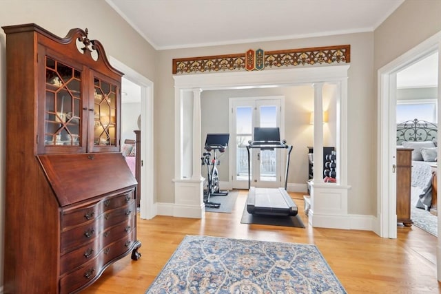 interior space with light wood-style flooring, ornamental molding, baseboards, and decorative columns