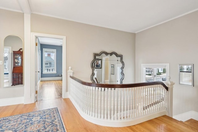 hall with baseboards, ornamental molding, an upstairs landing, wood finished floors, and arched walkways