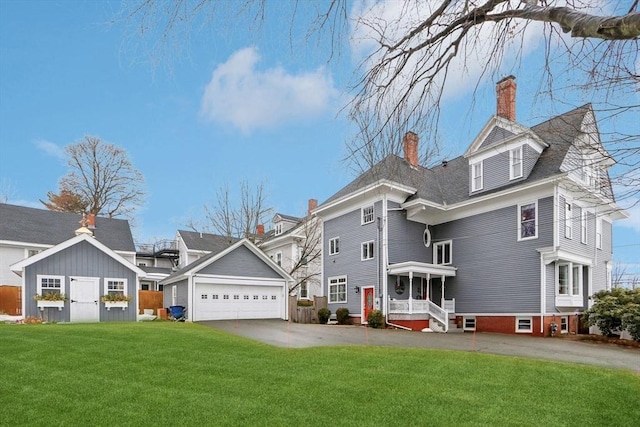 back of property with driveway, a porch, an attached garage, a yard, and a chimney