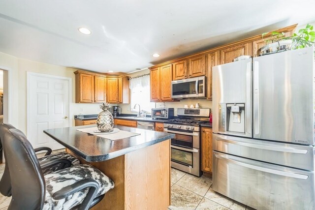 kitchen with brown cabinets, light tile patterned flooring, a kitchen bar, and stainless steel appliances