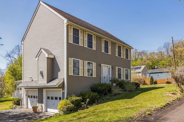 colonial inspired home featuring fence, an attached garage, a front lawn, and aphalt driveway