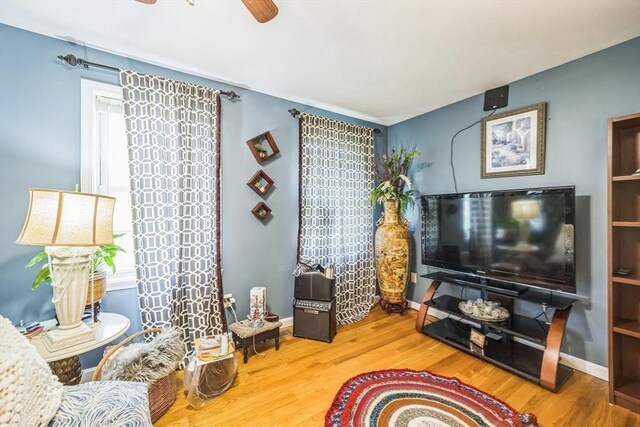 living area with baseboards, ceiling fan, wood finished floors, and a healthy amount of sunlight