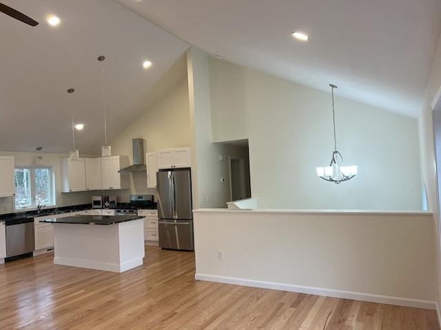 kitchen featuring a kitchen island, decorative light fixtures, white cabinets, stainless steel appliances, and wall chimney range hood