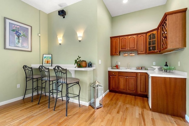 6 Bishop Ln, Middleton, MA 01949 - kitchen featuring glass insert cabinets, brown cabinetry, light wood-style flooring, and a kitchen bar