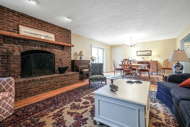 living room with hardwood / wood-style floors, a textured ceiling, an inviting chandelier, and a brick fireplace