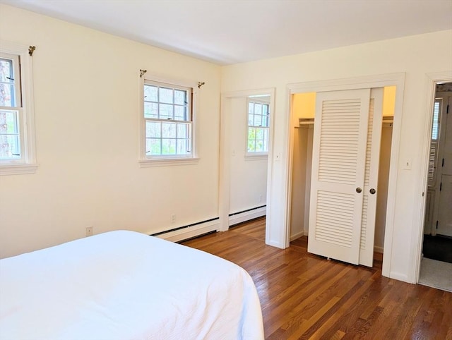 bedroom featuring baseboard heating, baseboards, dark wood-type flooring, and a closet