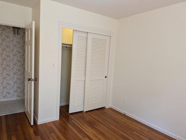 unfurnished bedroom with baseboards, a closet, and dark wood finished floors