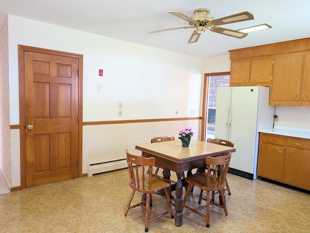 dining area featuring a wainscoted wall, light floors, a ceiling fan, tile walls, and baseboard heating