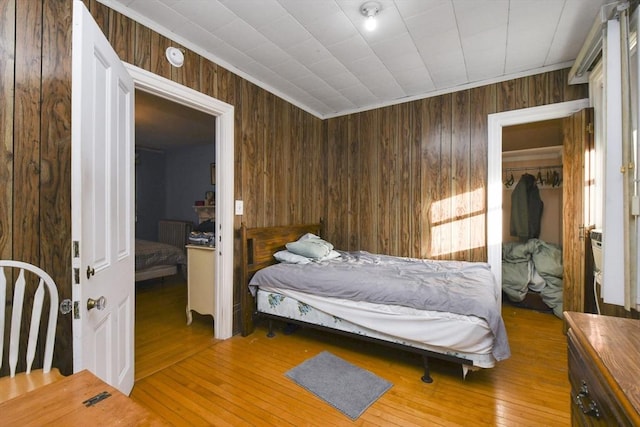 bedroom featuring a spacious closet, wooden walls, a closet, and light wood-type flooring