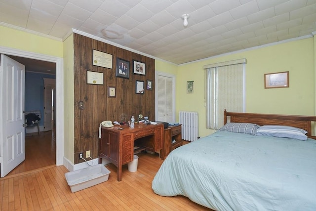 bedroom featuring light hardwood / wood-style flooring, radiator heating unit, ornamental molding, a closet, and wood walls