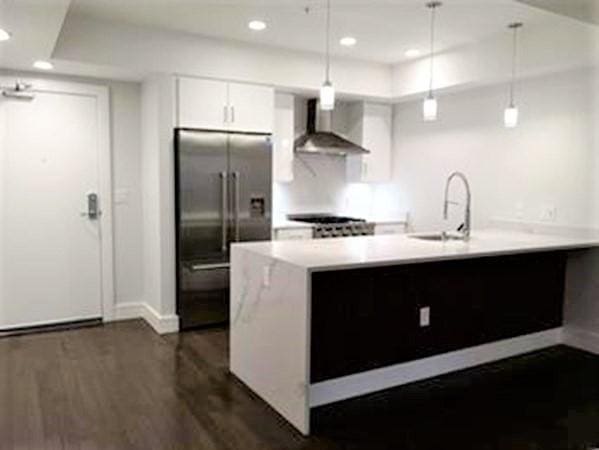 262 Monsignor Obrien Hwy Unit 503, Cambridge, MA 02141 - kitchen with wall chimney range hood, built in fridge, dark wood-style flooring, white cabinets, and light countertops