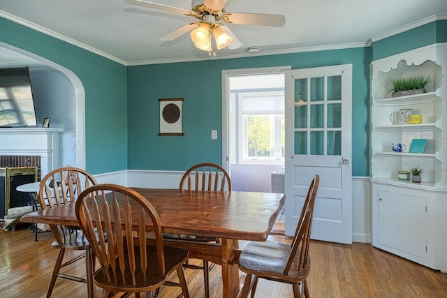 242 Furnace Brook Pkwy, Quincy, MA 02169 - dining room featuring wood finished floors, a brick fireplace, ornamental molding, a ceiling fan, and arched walkways