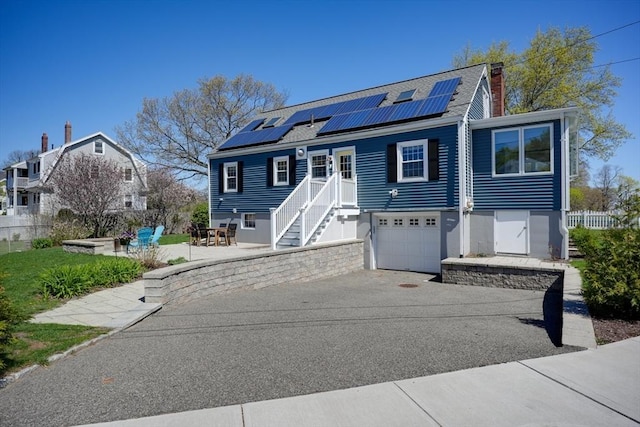 242 Furnace Brook Pkwy, Quincy, MA 02169 - view of front of property featuring asphalt driveway, roof mounted solar panels, an attached garage, a chimney, and a patio