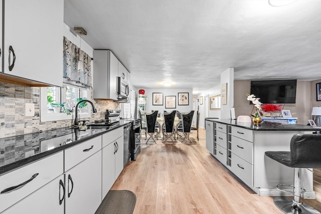 kitchen featuring tasteful backsplash, stainless steel appliances, sink, light hardwood / wood-style flooring, and white cabinets