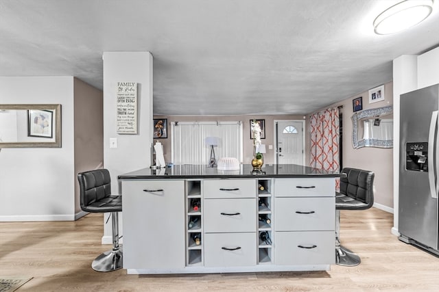 kitchen featuring stainless steel fridge with ice dispenser, a kitchen breakfast bar, light wood-type flooring, and white cabinetry