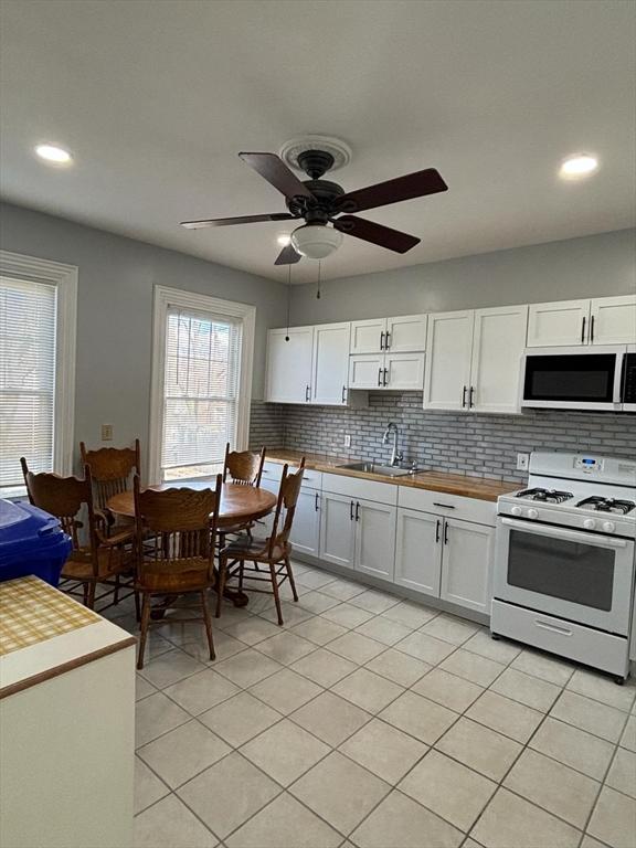 kitchen featuring white cabinetry, sink, backsplash, light tile patterned flooring, and white stove