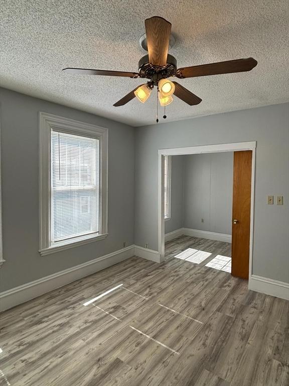 unfurnished room with ceiling fan, light wood-type flooring, and a textured ceiling