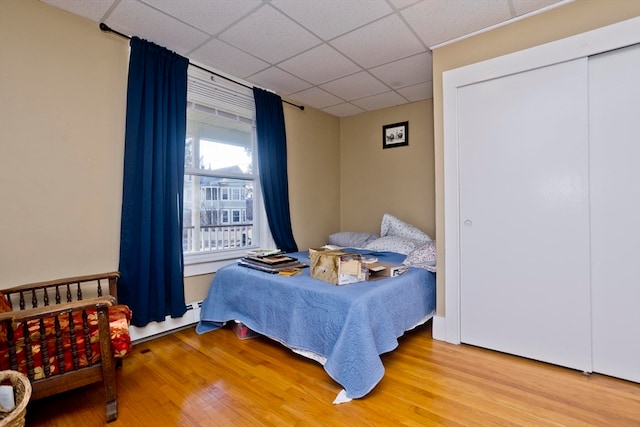 bedroom featuring hardwood / wood-style flooring, a paneled ceiling, a baseboard heating unit, and a closet