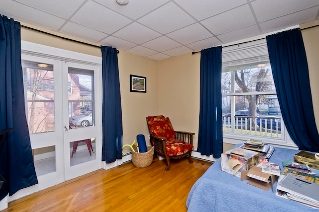 bedroom featuring french doors, a drop ceiling, hardwood / wood-style flooring, and multiple windows