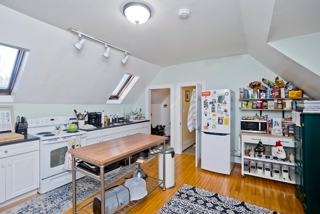 kitchen featuring white appliances, lofted ceiling with skylight, light wood-type flooring, a baseboard radiator, and white cabinetry