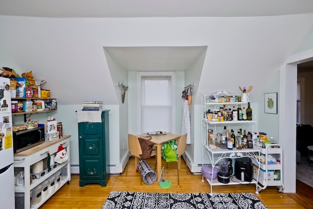 recreation room with light hardwood / wood-style floors, vaulted ceiling, and a baseboard radiator