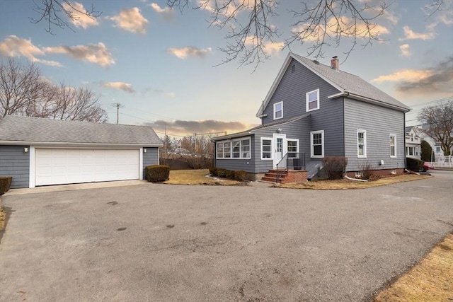 view of front of home featuring a shingled roof, an outbuilding, a detached garage, and a chimney