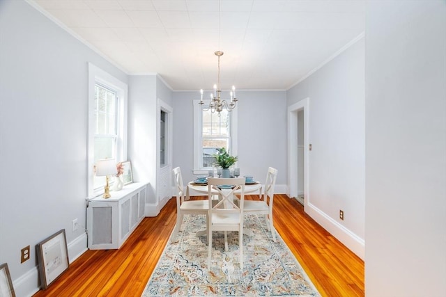 dining area with light wood-type flooring, baseboards, a notable chandelier, and ornamental molding