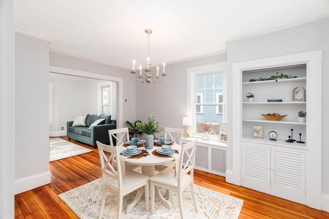 dining area with built in shelves, a chandelier, crown molding, and light wood-style flooring