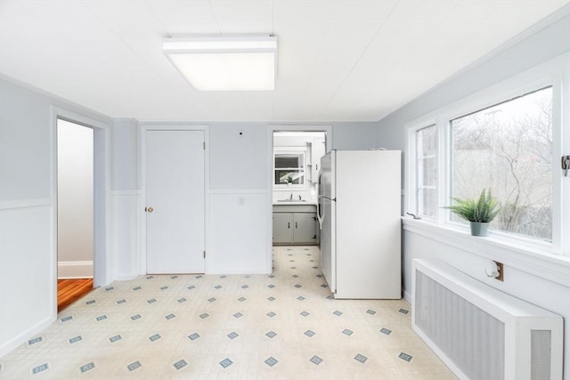 kitchen with light floors, radiator heating unit, a sink, and freestanding refrigerator