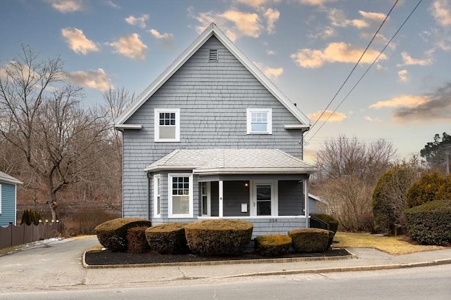 view of front facade featuring a shingled roof and fence