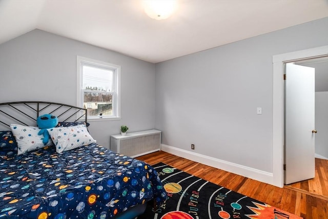 bedroom featuring lofted ceiling, radiator heating unit, baseboards, and wood finished floors