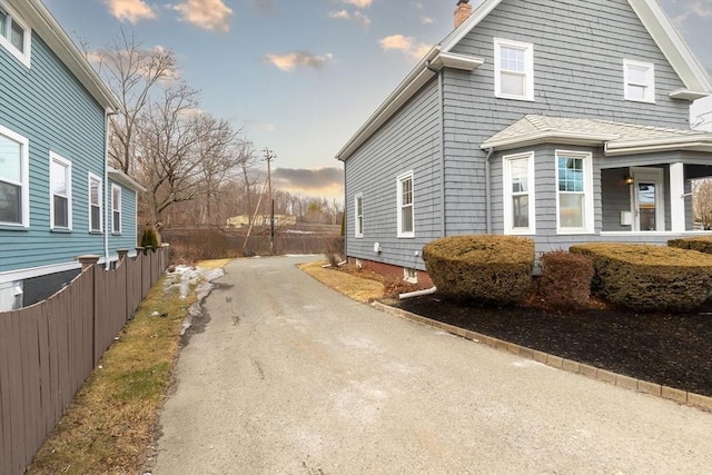 view of side of home featuring aphalt driveway, fence, and a chimney