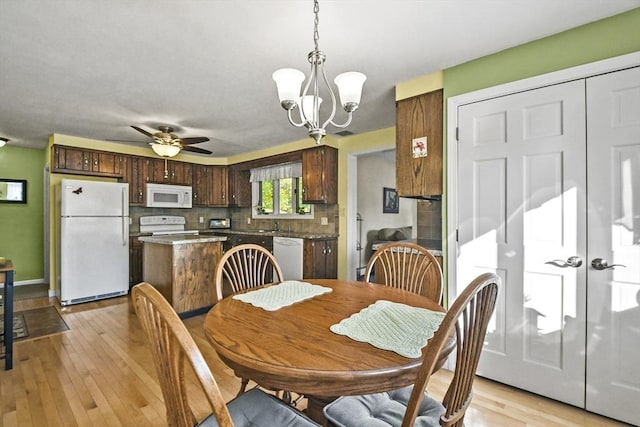 dining room featuring light wood finished floors, a chandelier, ceiling fan, and baseboards