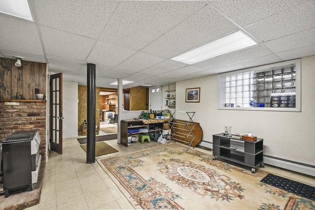 basement with a wood stove, a paneled ceiling, heating unit, and baseboard heating