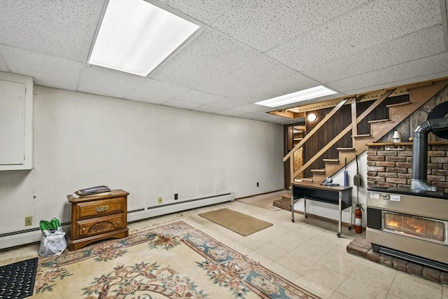 finished below grade area with a baseboard heating unit, a wood stove, stairway, and a paneled ceiling