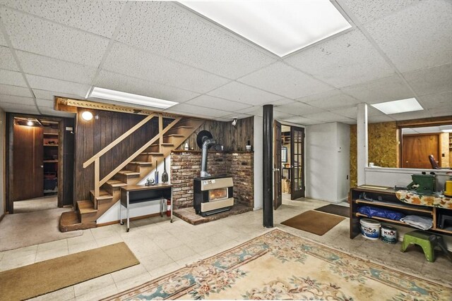 finished basement featuring a wood stove, a drop ceiling, and stairs