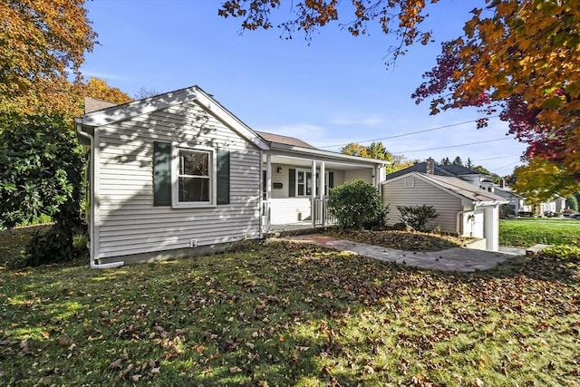 bungalow with covered porch, a front yard, and an outdoor structure