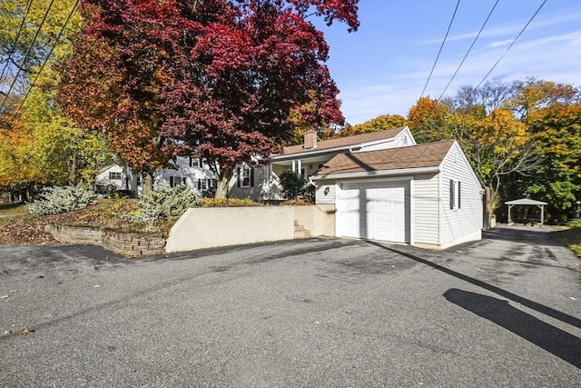 view of front facade featuring an attached garage, a chimney, and asphalt driveway