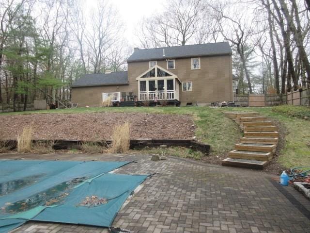 back of property featuring stairs, a sunroom, fence, a patio, and a covered pool