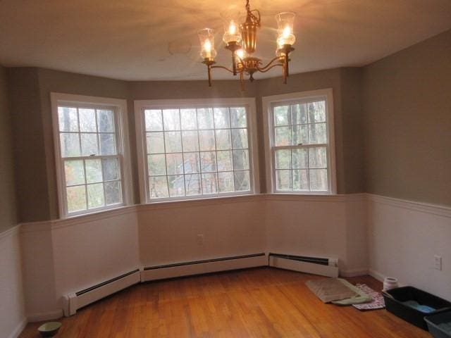 unfurnished dining area with wood finished floors, a chandelier, and baseboard heating