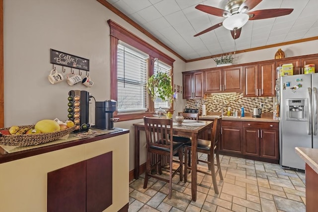 kitchen featuring ornamental molding, stone finish floor, backsplash, stainless steel fridge with ice dispenser, and ceiling fan