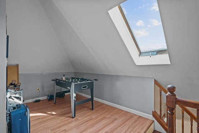 recreation room with lofted ceiling with skylight, baseboards, and wood finished floors